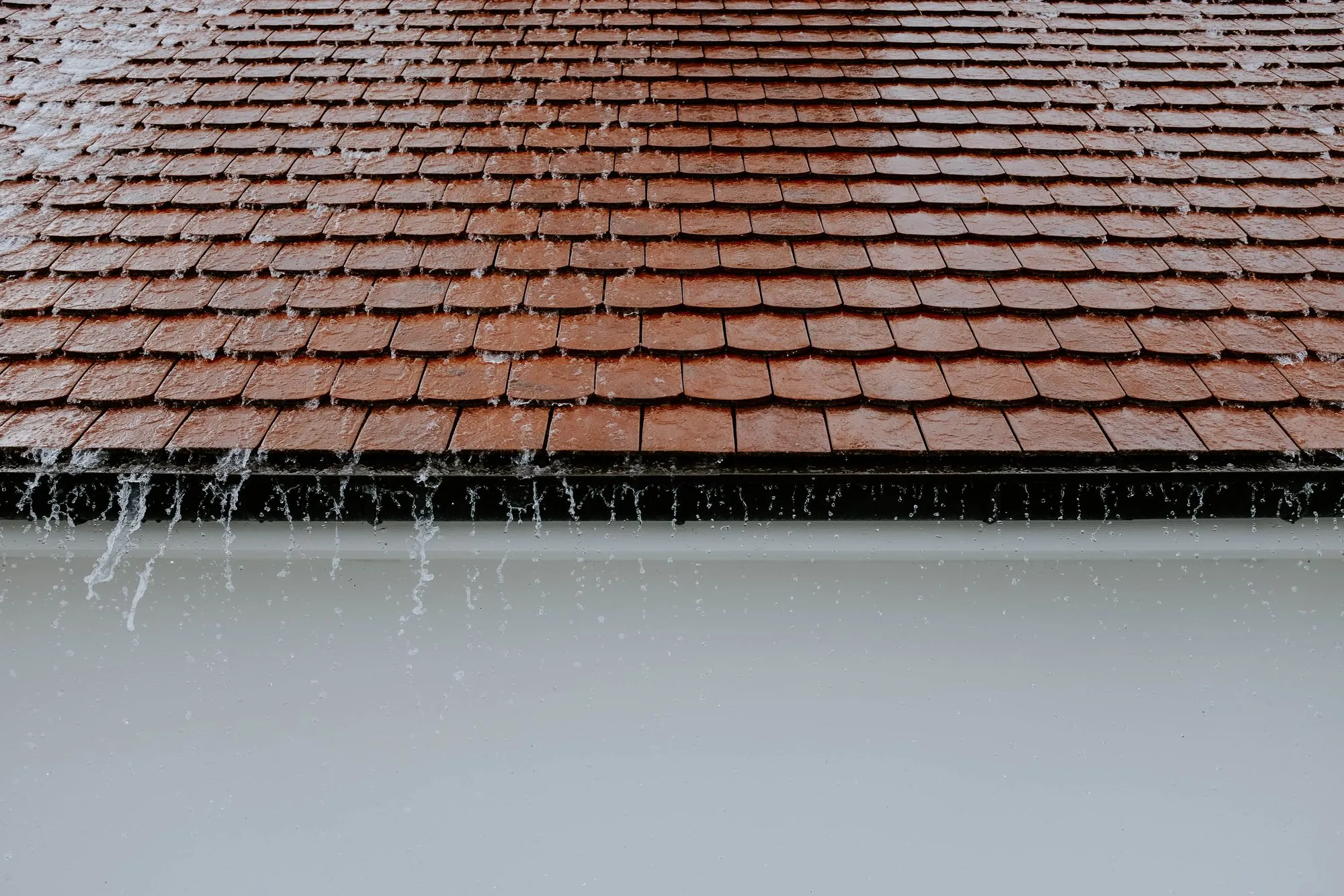 Rain spilling from a gutter beneath a roof edge
