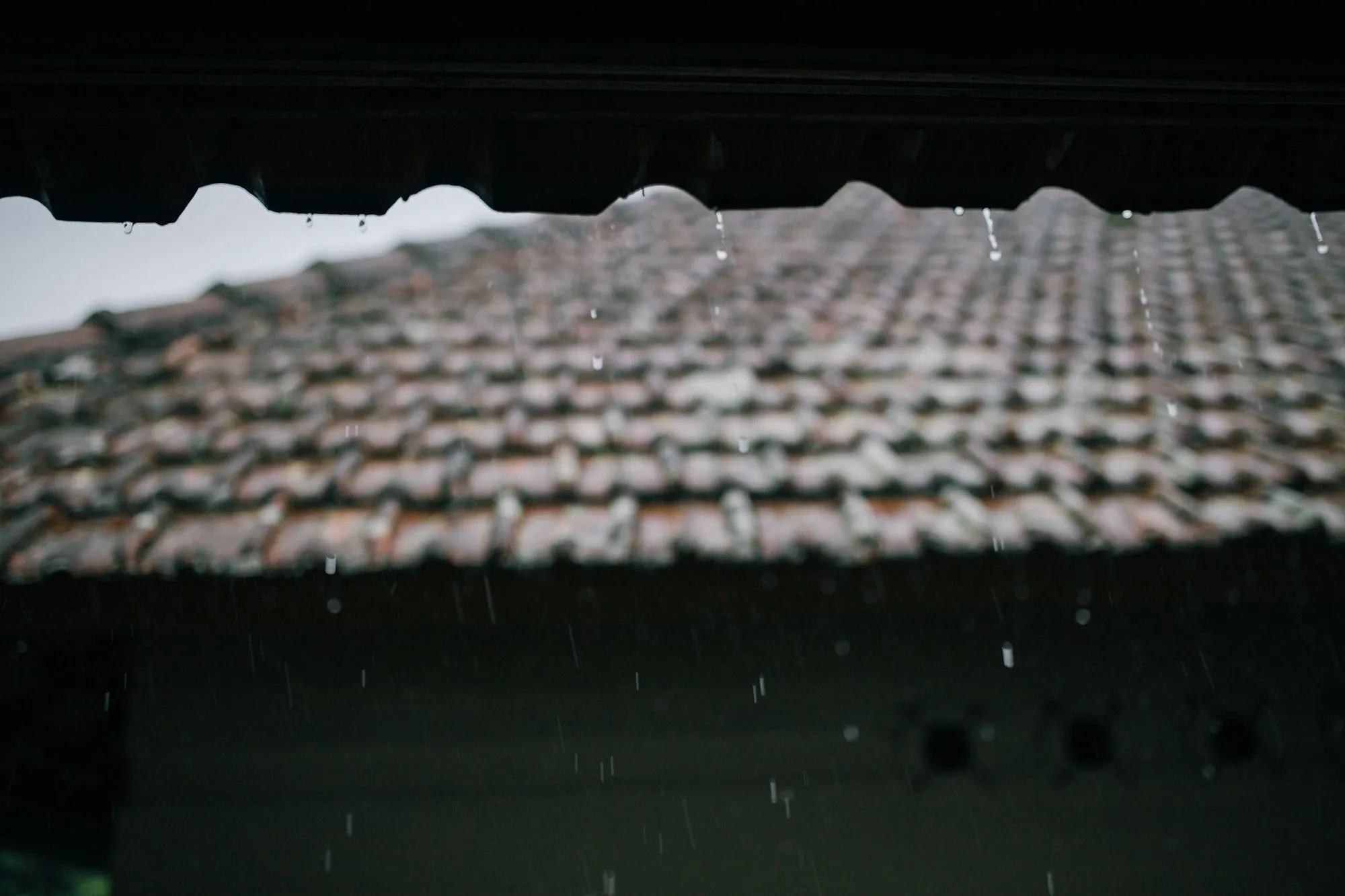 A tiled roof ridge seen along the slope in light rain
