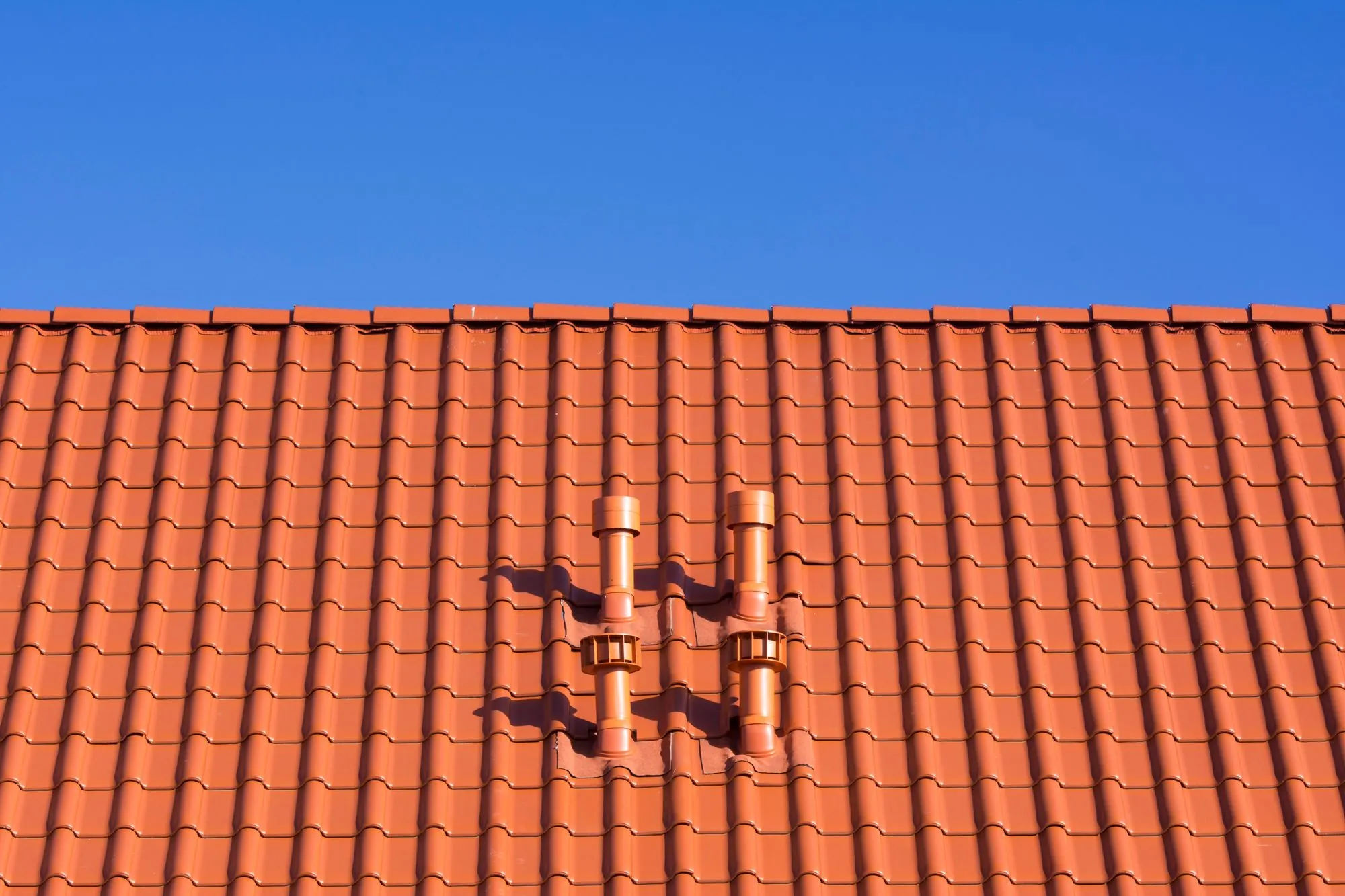 A tiled roof with two chimney pots under a bright sky