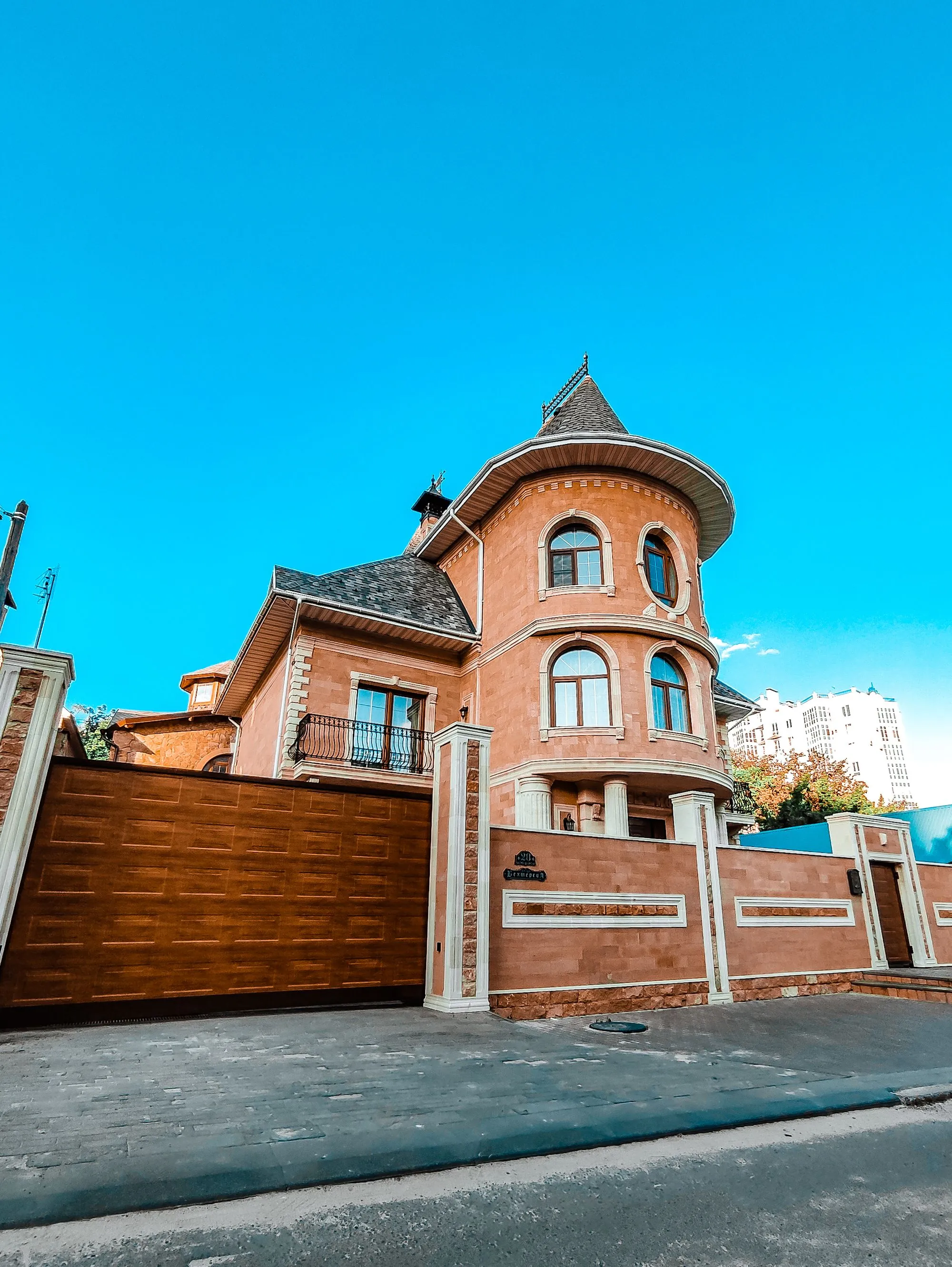 A brick house with a steep slate roof and turret against a clear sky